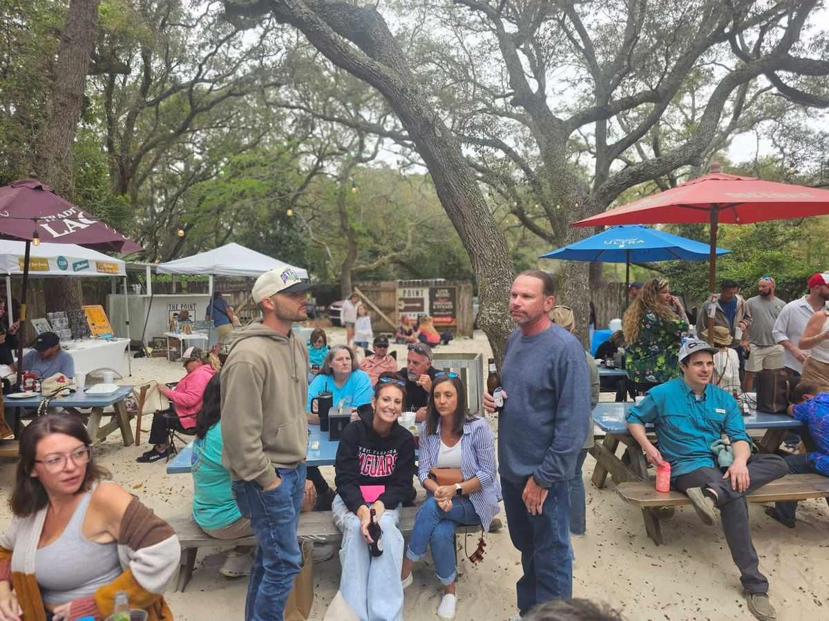 Crowd gathered at picnic tables under the oaks during a festival at The Point Restaurant Perdido, FL